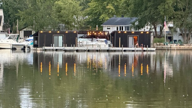 A waterfront property with docked boats, a small building with a door, and a house in the background.