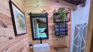 A wooden-paneled bathroom with a white sink, black cabinets, a mirror, a framed picture, a potted plant, towels, and a shower curtain.
