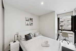 Een moderne hotelkamer met een opgemaakt bed, een bureau met stoel, en een raam met uitzicht op het gebouw.
