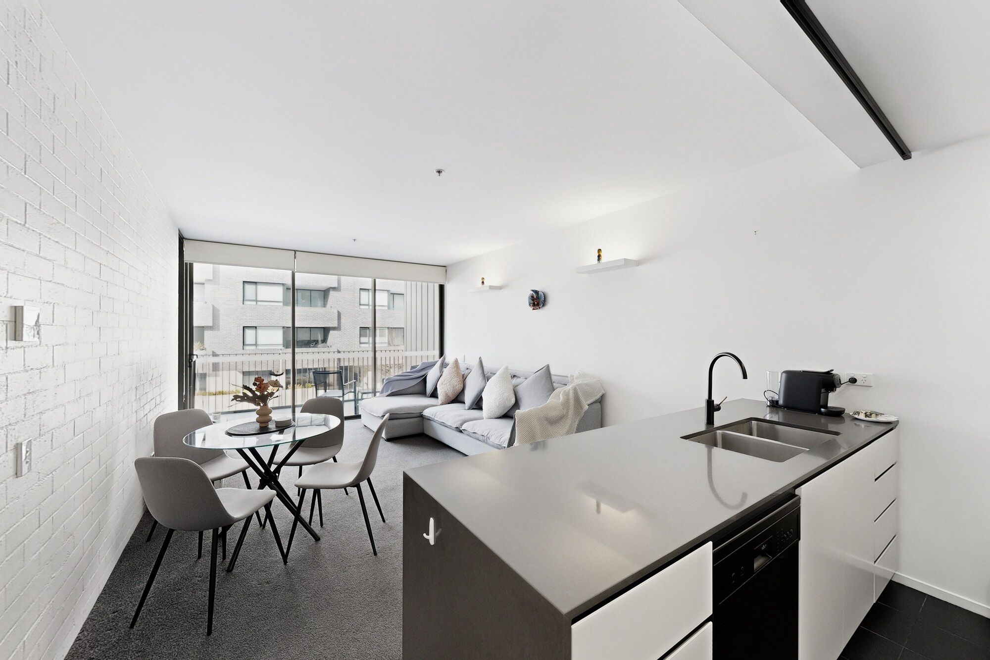 A modern kitchen with a central island, a dining area with a round table and chairs, and a living space with a sofa and a balcony.