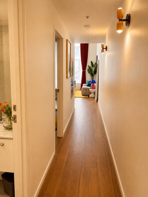 A hallway with wooden flooring, a door on the left, and a window with red curtains in the background. - Empire Theatre Loft |Your Colourful Melbourne Stay (Melbourne)