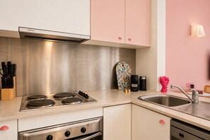 A kitchen with stainless steel appliances, a knife block, a colorful cutting board, and a sink. - Empire Theatre Loft |Your Colourful Melbourne Stay (Melbourne)