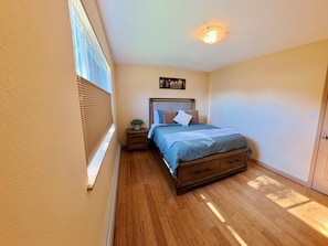 A bedroom with a wooden floor, a bed with a headboard, a bedside table with a plant, and a window with blinds. - Awesome 3-bedroom apartment in Anchorage perfect for your getaway (Anchorage)