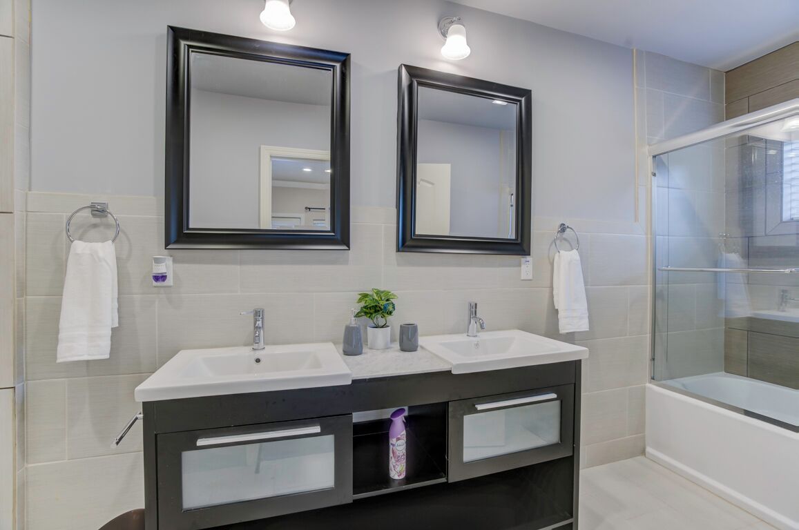 A bathroom with two sinks, a mirror, a shower, and a towel rack.