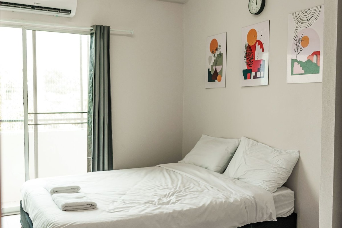 A bedroom with a bed, a window, an air conditioning unit, and wall art.
