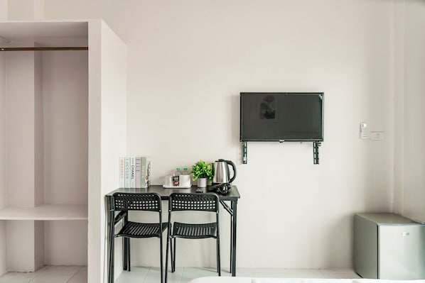 A compact room with a desk, two chairs, a television mounted on the wall, and a small refrigerator.