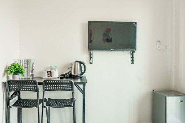 A kitchenette with a small table, two chairs, a kettle, a plant, and a TV mounted on the wall. - KID-DE HOUSE Bangsaen (Mueang Chon Buri District)