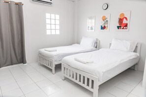A hotel room with two single beds, a window, a clock, and a wall-mounted air conditioner. - KID-DE HOUSE Bangsaen (Mueang Chon Buri District)