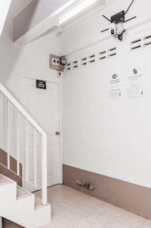 Une pièce propre et blanche, avec une porte portant l’inscription « SALLE 202 », une caméra de surveillance fixée au plafond et un panneau indiquant la présence d’un réseau Wi-Fi.