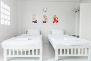 A bedroom with two beds, white bedding, a clock, and three wall art pieces.