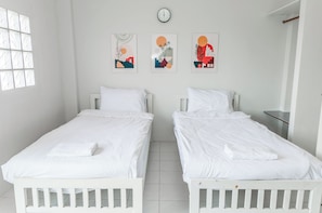 A room with two white beds, a clock on the wall, and three abstract paintings.