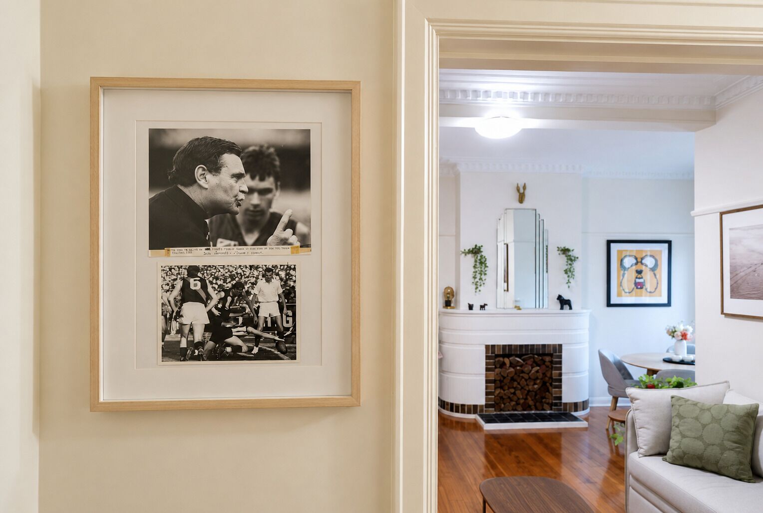A framed photograph of a sports event on the wall, a fireplace with a mantel, and a seating area with a sofa and a small table.