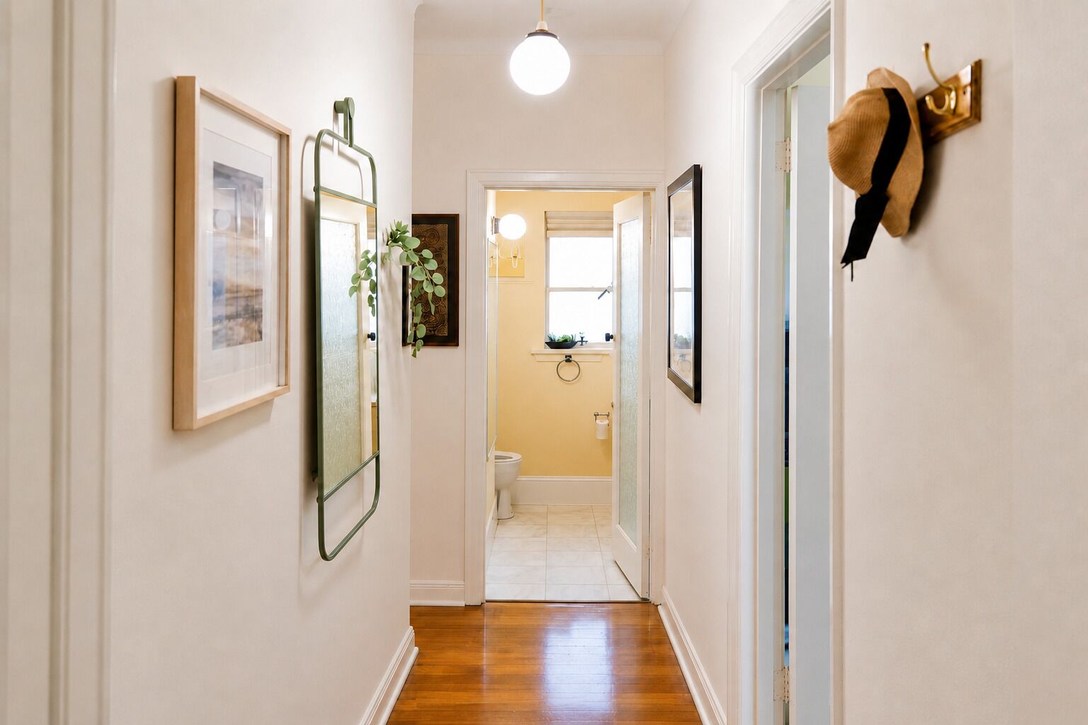 A hallway with framed pictures, a mirror, a plant, and a hat on the wall.