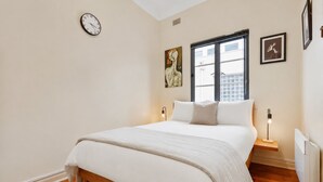 A bedroom with a bed, a clock, a window, and artwork on the walls. - Sophisticated East Melbourne Retreat by Ready Set Stay (East Melbourne)