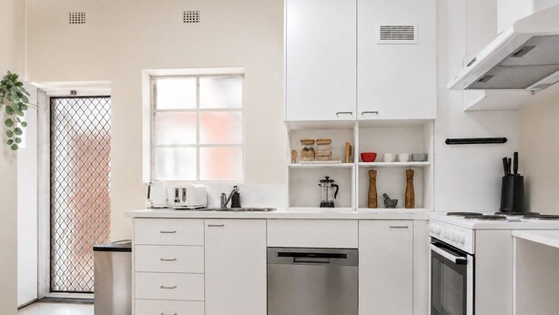 A modern kitchen with white cabinetry, a stainless steel dishwasher, a built-in oven, and a window with a view. - Sophisticated East Melbourne Retreat by Ready Set Stay (East Melbourne)