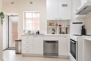 Een moderne keuken met witte kasten, een RVS vaatwasser, een inbouwoven en een raam met uitzicht.