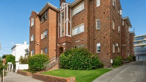 A multi-story brick building with a central staircase, a well-maintained lawn, and a gated driveway. - Sophisticated East Melbourne Retreat by Ready Set Stay (East Melbourne)