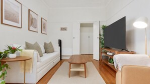 A modern living room with a sofa, coffee table, TV, and a flat-screen TV on a stand. - Sophisticated East Melbourne Retreat by Ready Set Stay (East Melbourne)
