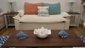 A living room with a beige sofa, a 'welcome' pillow, and decorative shells on a wooden coffee table. - Resort Style Condo w/ Pool & Outdoor BBQ!!! (Titusville)