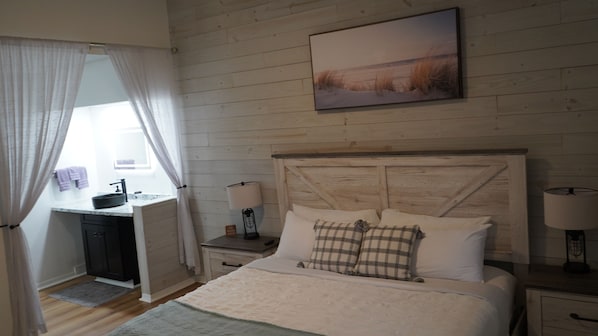 A bedroom with a wooden headboard, a bed with white bedding, a bedside table with a lamp, and a window with curtains.