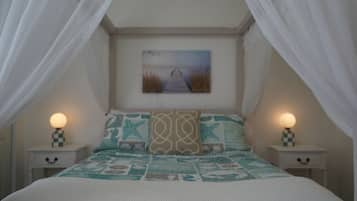 A bedroom with a bed, two bedside tables, a nightstand, a painting on the wall, and a canopy over the bed.