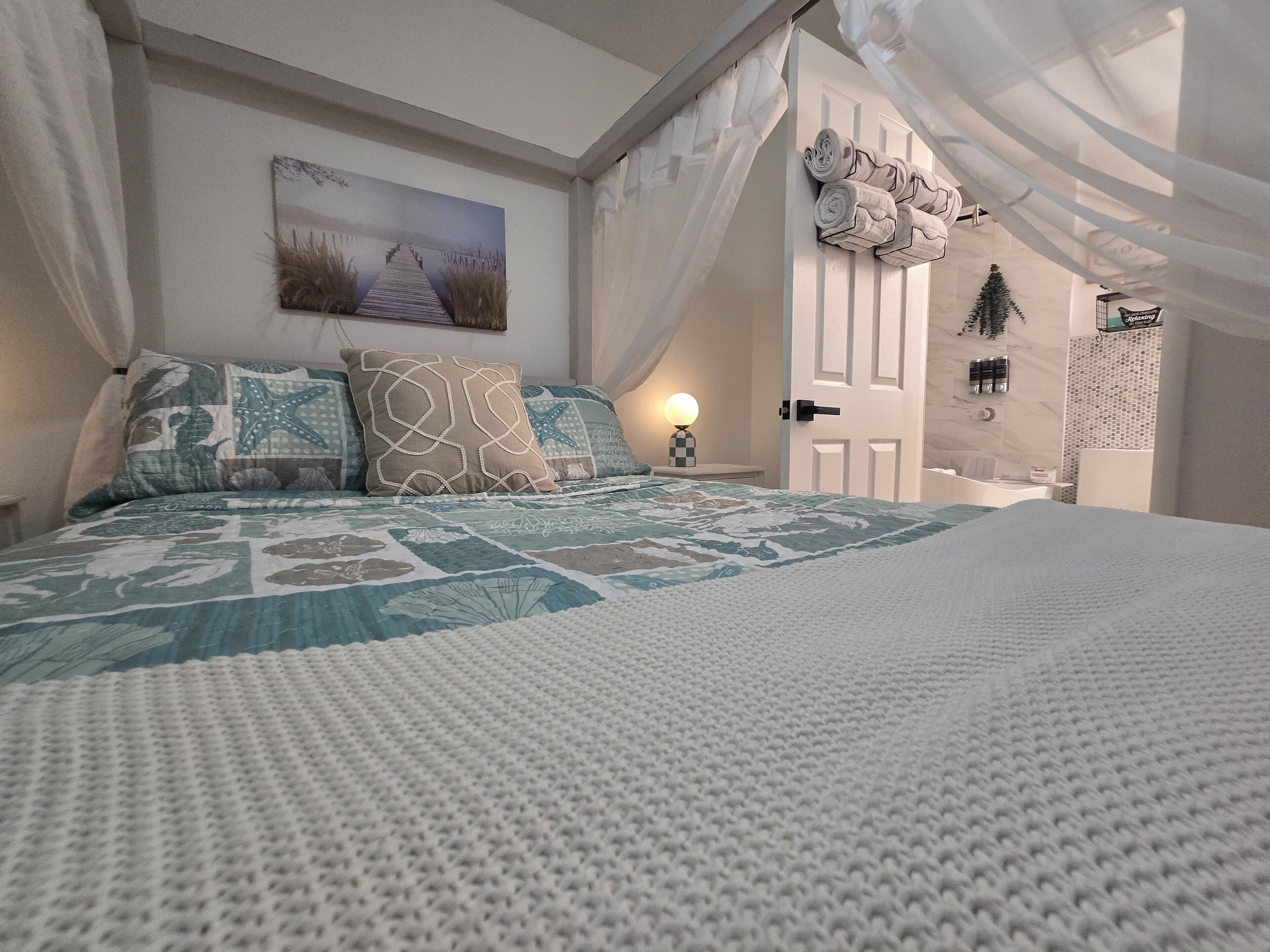 Ein Schlafzimmer mit einem großen Bett, einem Gemälde an der Wand und einer Tür zu einem anderen Raum.