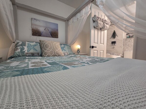 A bedroom with a large bed, a painting on the wall, and a door leading to another room.