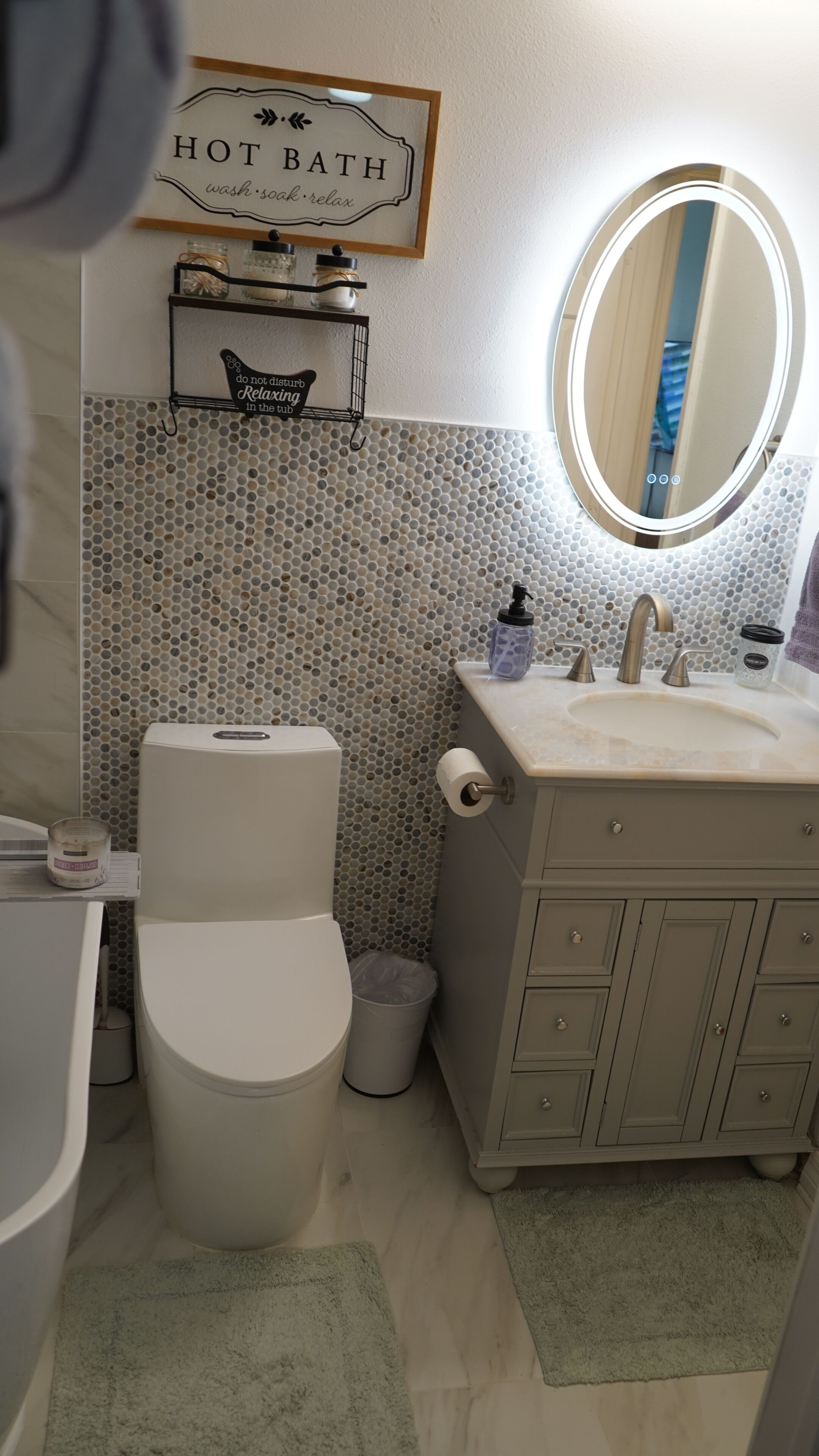 Ein Badezimmer mit Toilette, Waschbecken und Spiegel. Über dem Waschbecken befindet sich ein Schild mit der Aufschrift 'HEISSES BAD' und ein weiteres Schild mit der Aufschrift 'Bitte nicht stören. Entspannung in der Badewanne.'