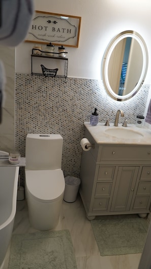 A bathroom with a toilet, sink, and mirror. There is a sign above the sink that reads 'HOT BATH' and another sign that says 'do not disturb Relaxing in the tub'.