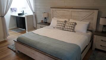 Une chambre à coucher avec un lit en bois, une table de chevet avec une lampe, un petit bureau avec un lavabo et une fenêtre avec des rideaux.