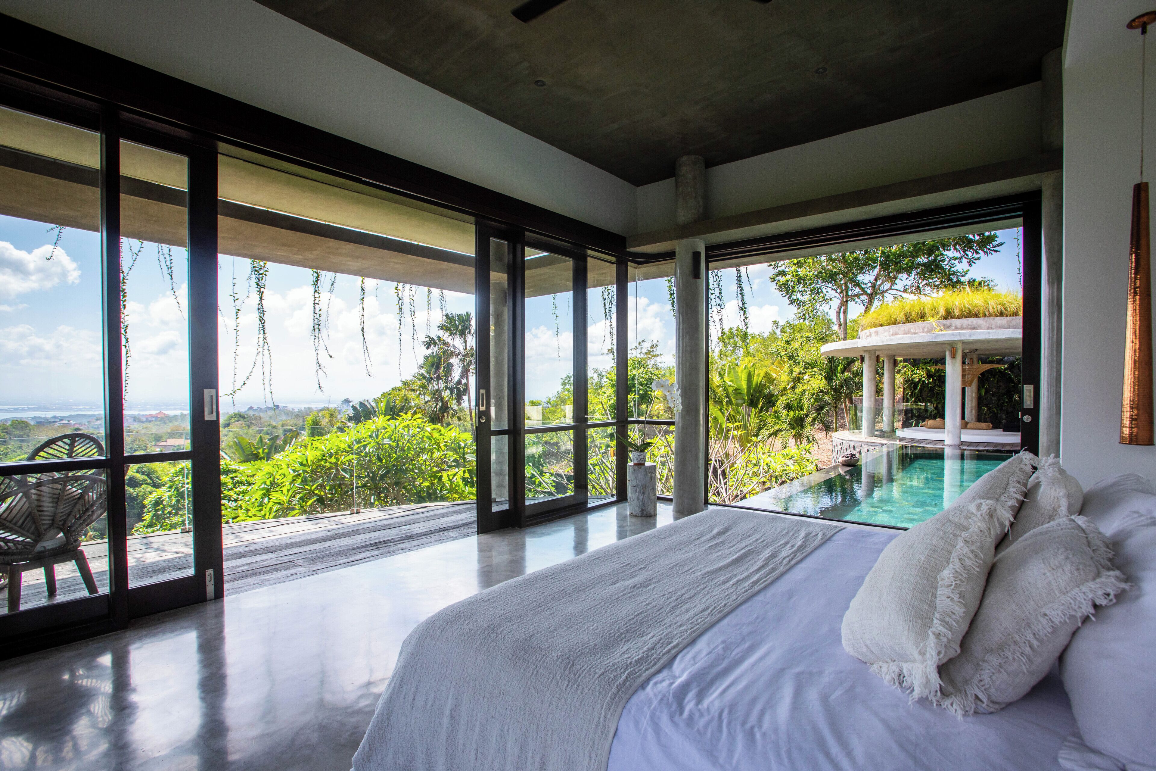 Une chambre avec un grand lit, une vue sur la piscine et un balcon avec un fauteuil.