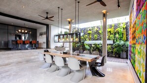 Un comedor moderno con una mesa larga, varias sillas, ventiladores de techo y vistas a zonas verdes.