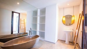 Un baño moderno con una bañera independiente grande, un lavabo blanco y un espejo con marco redondo.