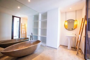 Ein modernes Badezimmer mit einer großzügigen Freisitzbadewanne, einem weißen Waschbecken und einem Spiegel mit rundem Rahmen.