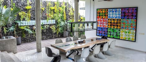A modern meeting room with a glass-top table, white chairs, and a colorful abstract art piece on the wall.