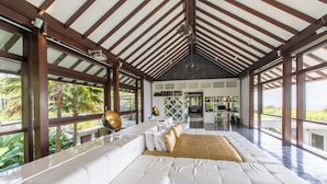 Amplia sala de estar con un sofá blanco grande, una mesa de centro y una chimenea. Se aprecia una vista de un jardín exuberante a través de amplios ventanales.