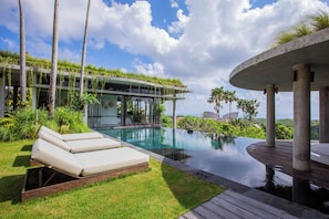 Ein moderner Poolbereich mit einem verglasten Infinity-Pool, Liegestühlen und üppiger Bepflanzung.