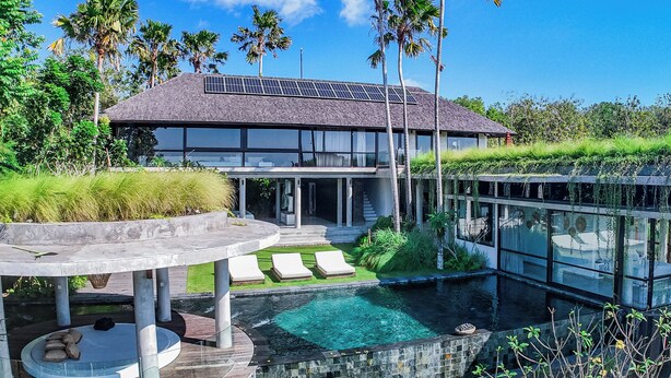 Una casa moderna con piscina, paneles solares y abundante vegetación.