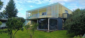 A two-story building with a balcony and a covered outdoor area. - Relax, Coastal and Warm-Top Deck Beach House (Pataua South)