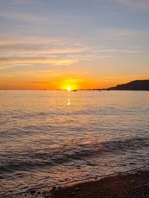 A sunset over a calm sea with a rocky coastline. - Relax, Coastal and Warm-Top Deck Beach House (Pataua South)