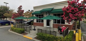 Um Starbucks com área externa, fachada de tijolos e um estacionamento ao fundo.