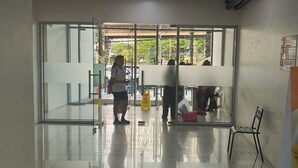 Corredor com porta de vidro que dá para área externa, aviso de chão molhado e placa indicando praça de alimentação.