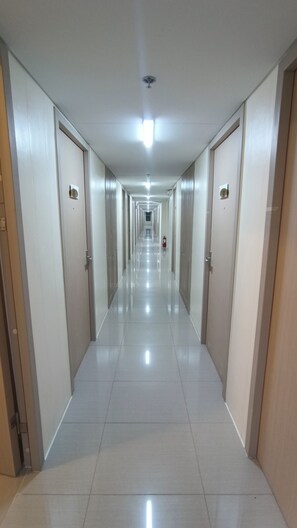 Un pasillo largo y estrecho con puertas a ambos lados, piso de baldosas y una lámpara en el techo.