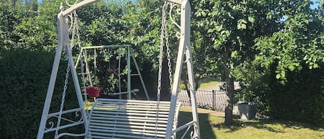 A metal swing set with a bench, surrounded by a brick pathway and greenery.