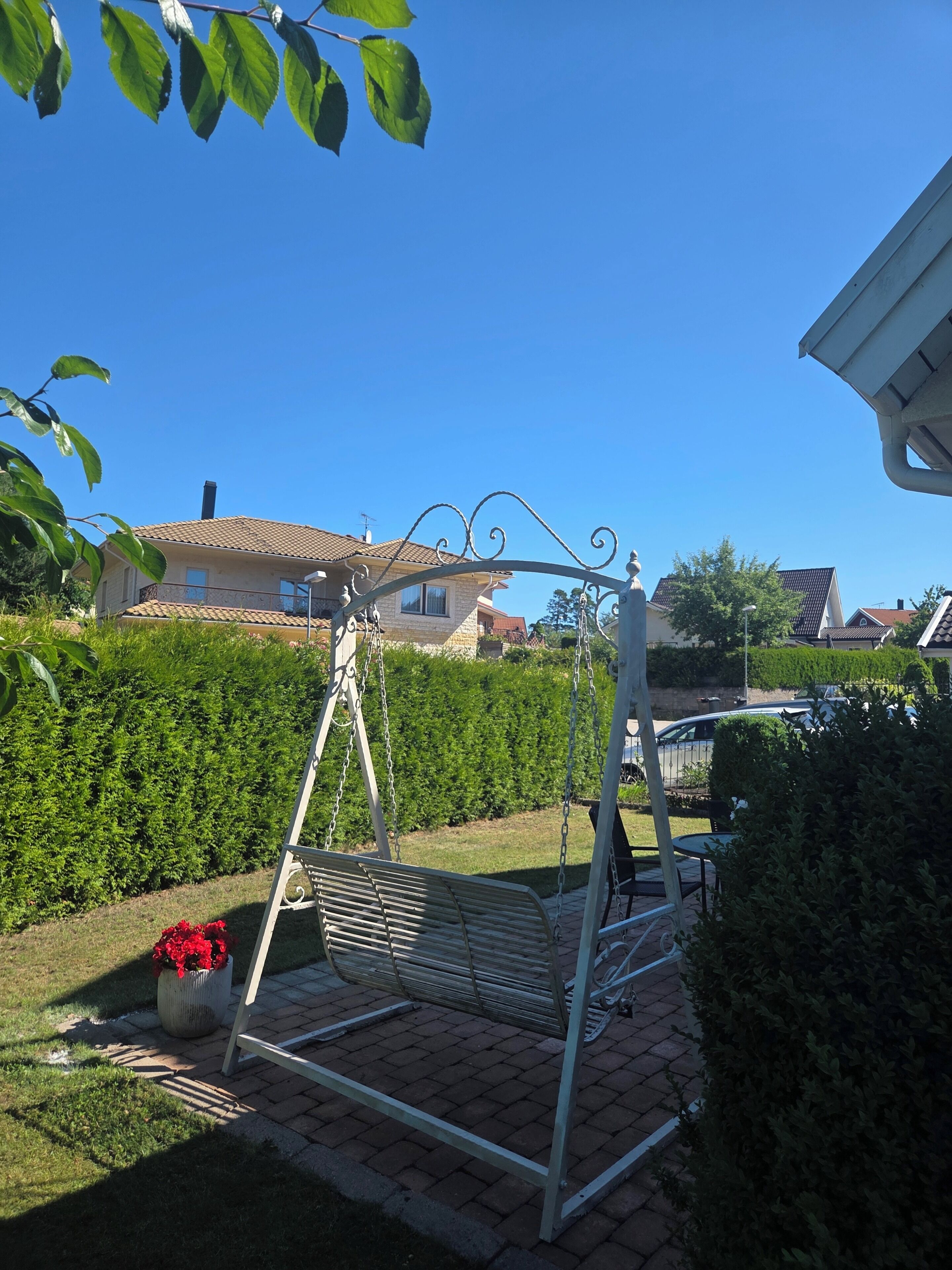 A garden with a swing set, a hedge, and a house in the background.
