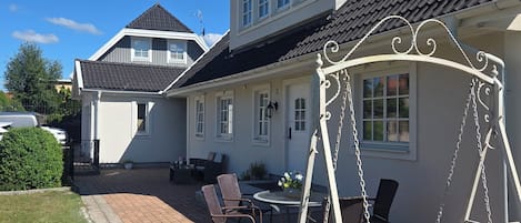 A residential property with a patio area featuring a swing set, outdoor seating, and a potted plant.