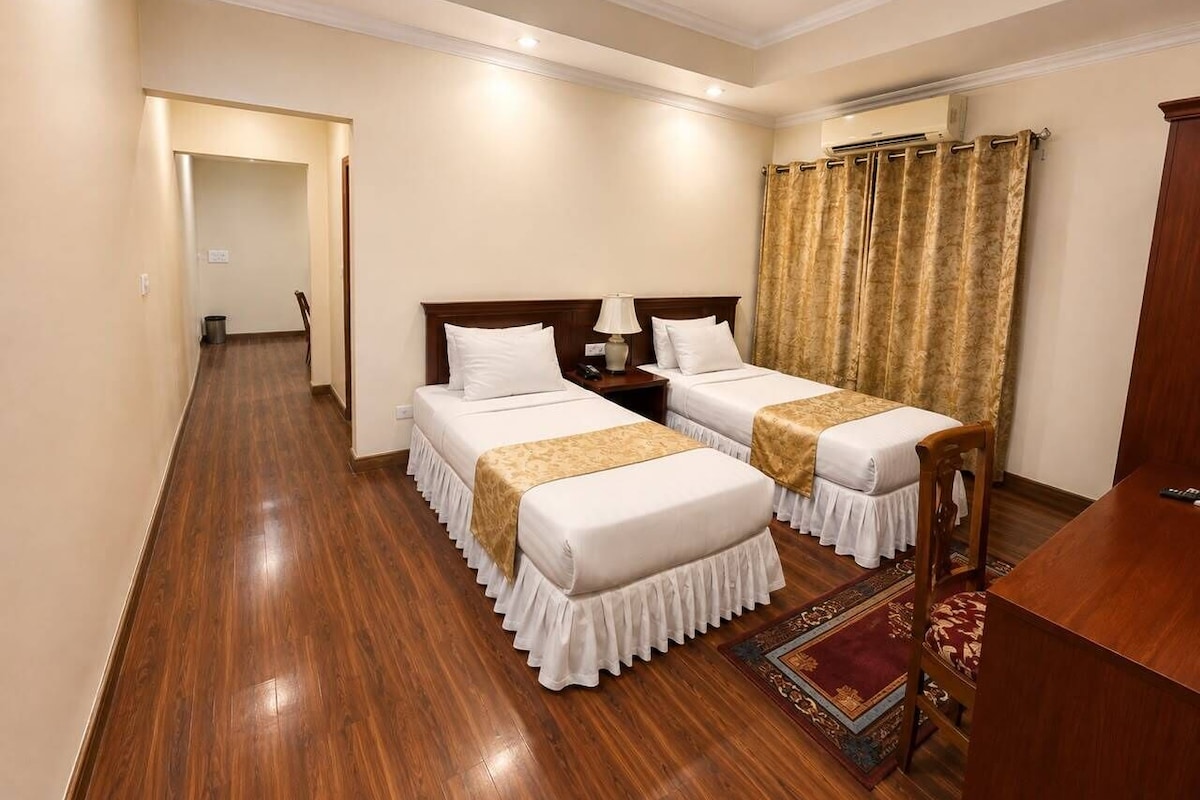 A hotel room with two beds, a desk, a chair, a rug, and a curtain.