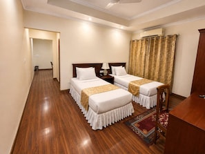 A hotel room with two beds, a desk, a chair, a rug, and a curtain. - The Orchid Hotel (Phuentosholing)