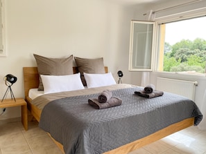 A bedroom with a bed, pillows, a bedside lamp, a window, and a view of greenery. - Beautiful villa with pool and close to a village (Lorgues)