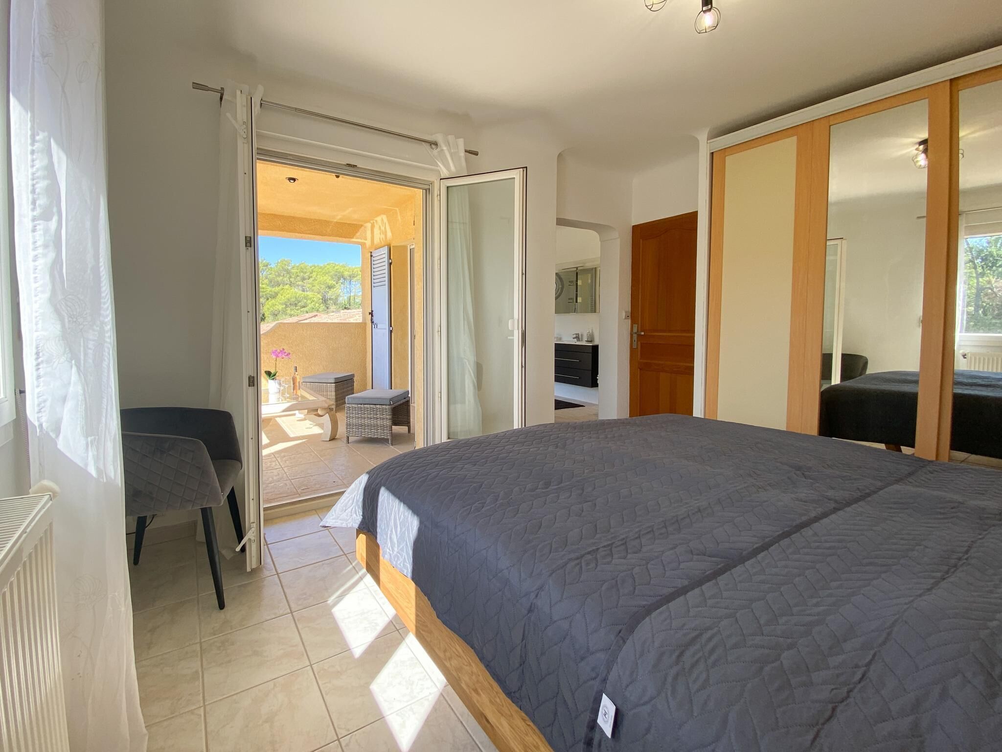 Un dormitorio con cama, escritorio, silla, armario y baño visible a través de una puerta abierta.